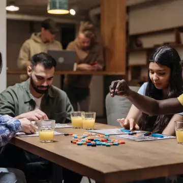Friends playing a board game at a wooden table, with glasses of juice.